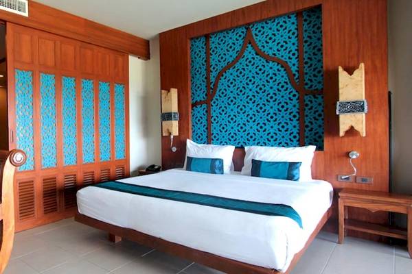 Innenansicht eines Zimmers im Rawai Palm Beach Resort mit einem Bett, Kissen und blauen Wandmustern.