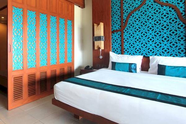 Innenansicht eines Zimmers im Rawai Palm Beach Resort mit einem Bett, blauen Kopfkissen und blau-gemusterten Wandverkleidungen.