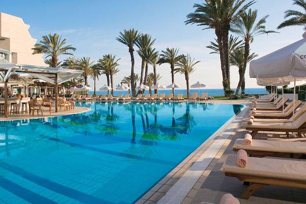 Poolbereich des Pioneer Beach Hotel mit Sonnenliegen und Palmen am Meer