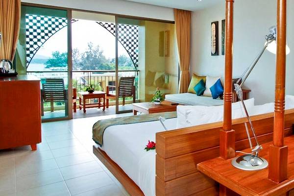 Innenansicht eines Zimmers im Rawai Palm Beach Resort mit Bett, Schreibtisch, Lampen und Balkonzugang.