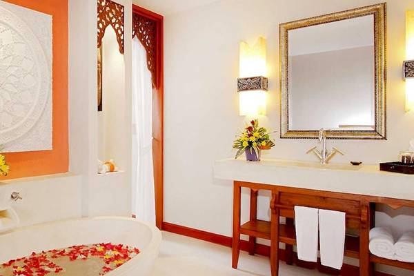 Badezimmer im Rawai Palm Beach Resort mit Badewanne, Blumen, Spiegel und Waschbecken.