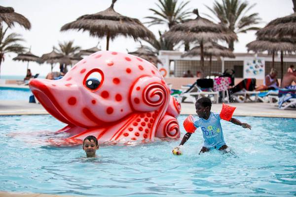 Zwei Kinder spielen im Pool mit einem großen roten Fischspielzeug im El Mouradi Djerba Menzel Hotel.