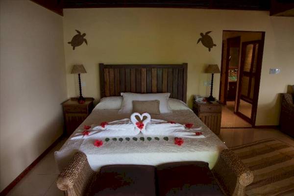 Ein Schlafzimmer mit einem Bett, auf dem zwei weiße Schwäne und rote Blumen liegen, neben zwei Nachttischen mit Lampen.