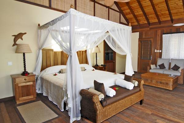 Schlafzimmer im Cerf Island Resort mit Himmelbett, Korbsofa und Dekor.