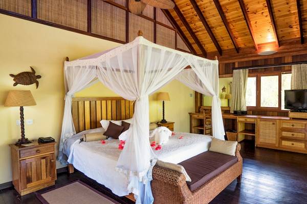 Schlafzimmer im Cerf Island Resort mit vier Poster Bett, Nachttischen, Fernseher, und Holzmöbeln.