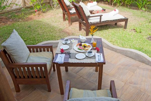 Frühstückstisch im Garten des Cerf Island Resorts mit Blick auf Liegestühle und Pflanzen.