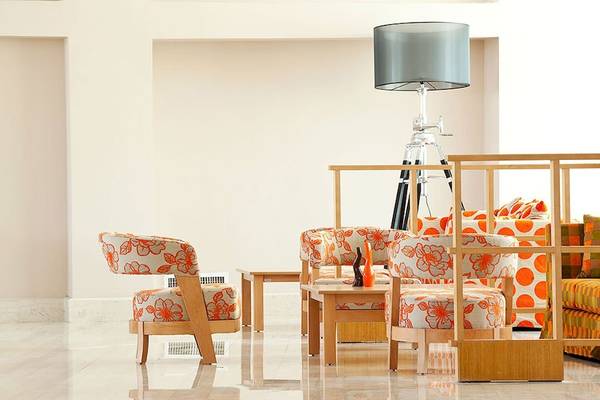 Lobby-Bereich des Lindos Bay Hotels mit orangefarbenen Stühlen und einem silbernen Lampenschirm.