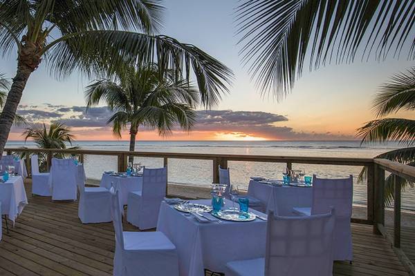 Sonnenuntergang am Strand des Victoria Beachcomber Resort & Spa mit Palmen und Tischen im Freien