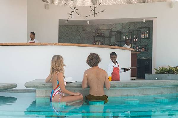Gäste sitzen am Pool-Barbereich des Victoria Beachcomber Resorts & Spa mit Barkeepern im Hintergrund.
