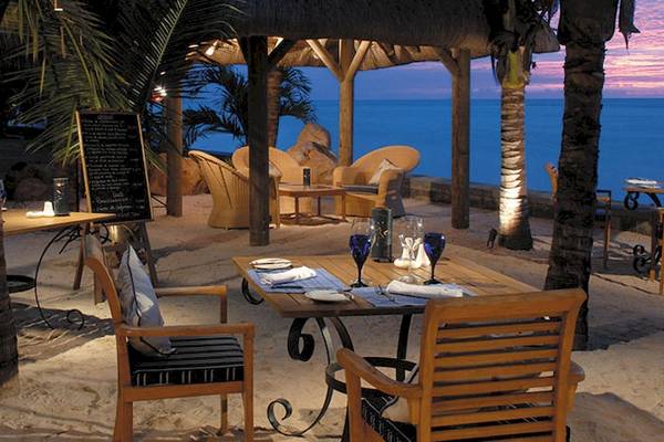Abendessen im Freien am Strand des Victoria Beachcomber Resorts & Spa mit Tischen, Stühlen und Palmen.