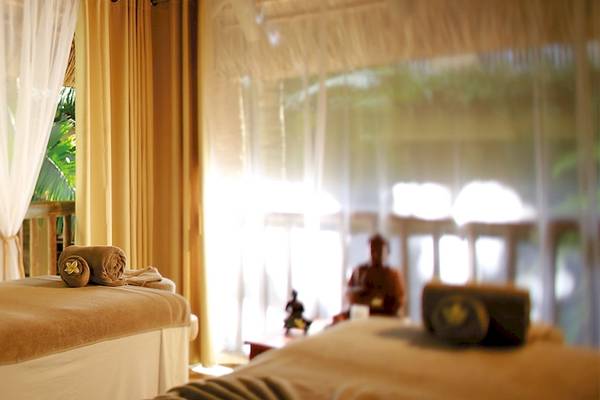 Behandlungsraum im Victoria Beachcomber Resort & Spa mit zwei Massagebetten und gelben Vorhängen.