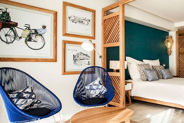 Innenansicht eines Schlafzimmers im Victoria Beachcomber Resort & Spa mit einem Bett, zwei blauen Stühlen und kunstvollen Holzwänden.