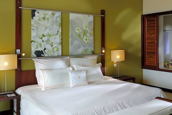 Schlafzimmer im Victoria Beachcomber Resort & Spa mit Bett, Kissen, Lampen und Fenstern.