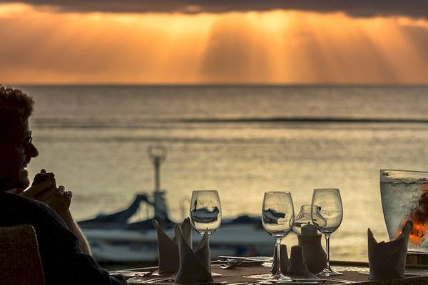 Ein Paar sitzt bei Sonnenuntergang am Tisch vor dem Meer mit Getränken und Wein.