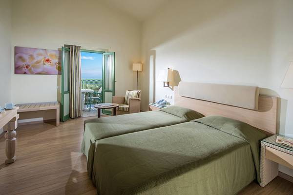 Zimmer im Silva Beach Hotel mit zwei grünen Betten, einem Balkon, einem Tisch und einem Stuhl.