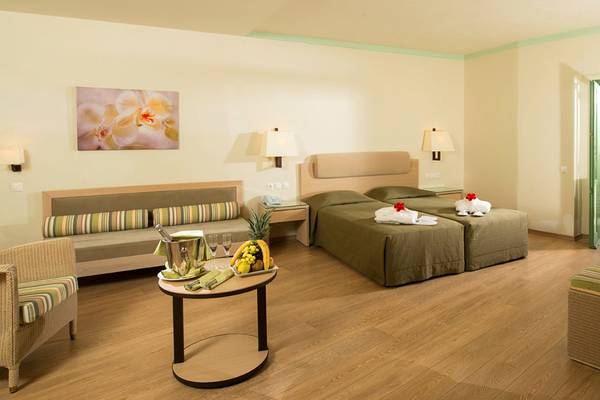 Doppelzimmer im Silva Beach Hotel mit Meerblick, zwei Betten, Tisch mit Früchten, Sofa und Balkon.