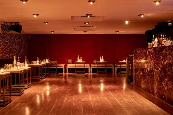 Ein Hotelbarbereich mit einer roten Wand und einem Holzboden, mit Tischen, Stühlen und runden Hockern, die mit Kissen bedeckt sind.