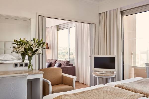Innenansicht eines Zimmers im Grecian Park Hotel mit einem Bett, einem Schreibtisch und einer Couch.