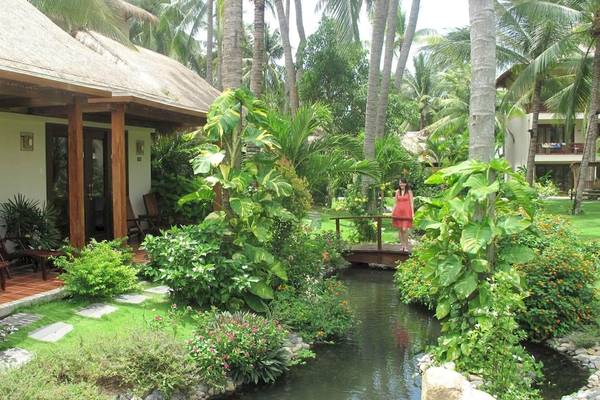 Villa im Bamboo Village Beach Resort mit Garten und Wasserlauf, eine Frau in einem roten Kleid steht auf der Brücke.