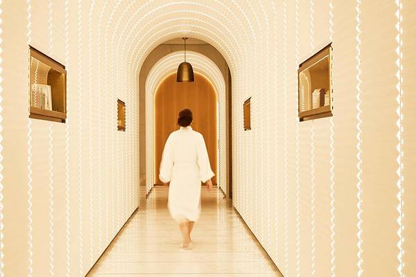 Eine Frau in einem weißen Bademantel geht durch den Eingang des Spas im Raffles The Palm Dubai.
