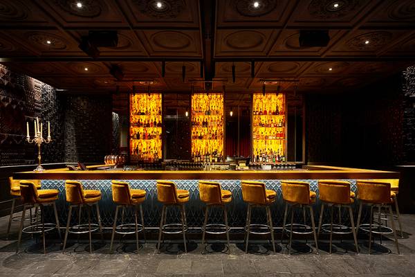 Bar-Szene im Raffles The Palm Dubai mit gelben Barhockern und einer Theke voller alkoholischer Getränke.