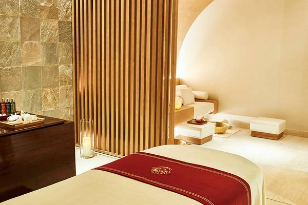 Spa-Behandlungsraum im Raffles The Palm Dubai mit Holzelementen, Sitzgelegenheiten und einem Tisch mit Wellnessprodukten.