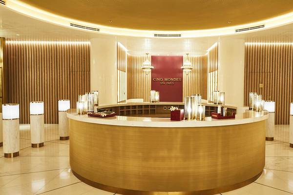 Empfangsbereich des Cing Mondes Spa im Raffles The Palm Dubai mit goldenem Tresen und weißen Säulen.