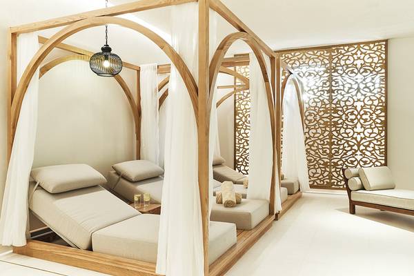 Spa-Lounge-Bereich im Raffles The Palm Dubai mit hölzernen Liegen, weißen Vorhängen und einer goldenen Wand.