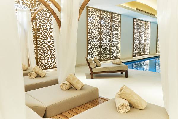 Poolbereich mit Lounges im Raffles The Palm Dubai Hotel, umgeben von blauem Wasser und goldenen Wandmustern.