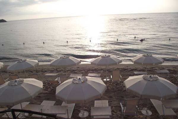Ein Blick auf den Strand von Baia Di Nora mit vielen Sonnenschirmen und Liegen am Meer.