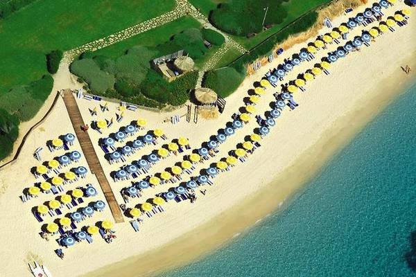 Luftperspektive des Baia Di Nora Hotels mit vielen Sonnenschirmen und Liegen am Strand.