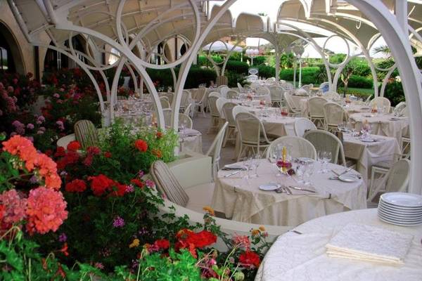 Außenbereich des Baia Di Nora Restaurants mit gedeckten Tischen und farbenfrohen Blumen.