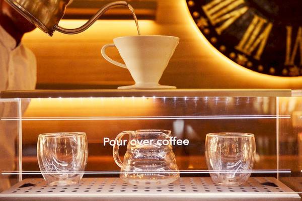 Kaffee wird in ein Glas gegossen, während eine Kanne und zwei Gläser darauf warten.