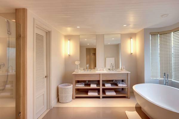 Innenansicht des Badezimmers im LUX Belle Mare Resort & Villas mit Badewanne, Waschbecken und Spiegeln.