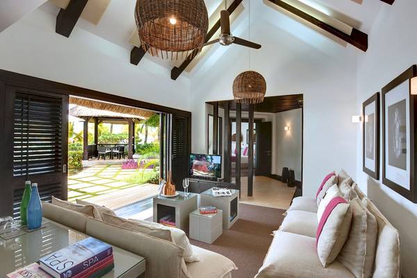 Innenansicht des Wohnzimmers im LUX Belle Mare Resort & Villas mit offener Terrasse, Fernseher, Sofas und Lampen.