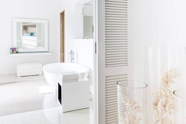 Das Badezimmer des LUX Belle Mare Resort & Villas mit einer weißen Badewanne, Spiegel und weißen Möbeln.