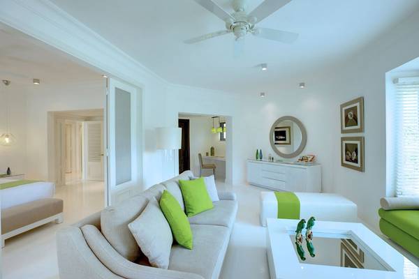Innenraum des LUX Belle Mare Resort & Villas mit weißen Möbeln, grünen Kissen und einer weißen Deckenventilator.