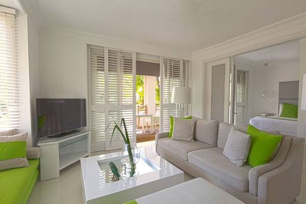 Wohnzimmer-Innenansicht des LUX Belle Mare Resort & Villas mit weißen Möbeln, grünen Kissen und einem Fernseher.