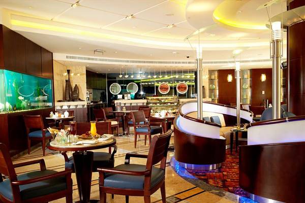 Innenansicht des Restaurants im Swissotel Al Murooj Dubai mit Tischen, Stühlen und einer großen Aquarienwand.