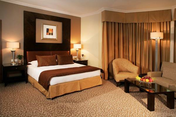 Hotelzimmer im Swissotel Al Murooj Dubai mit Doppelbett, Sesseln, Tisch und Früchten.