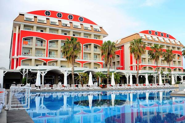 Außenansicht des Orange County Belek - Family Concept Hotels mit rotem Gebäude, Swimmingpool und Sonnenliegen.