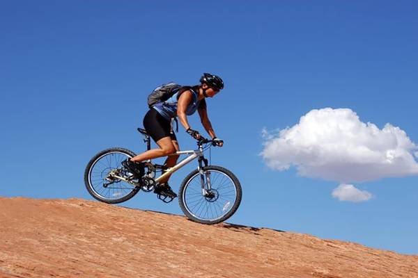 Frau mit Fahrrad auf einem Berg, im Himmel ist eine Wolke sichtbar