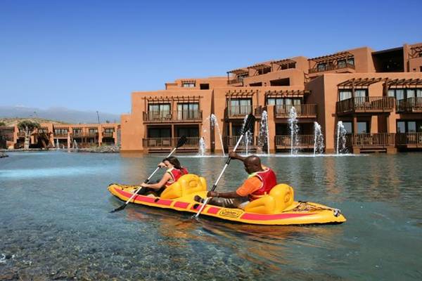 Zwei Personen paddeln in einem gelben Schlauchboot auf dem Wasser vor dem Barcelo Tenerife Hotel.