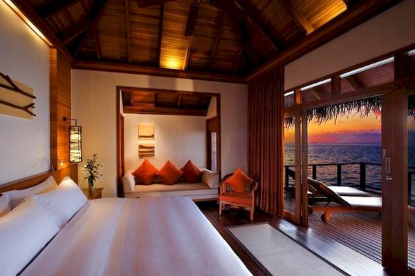 Schlafzimmer im Sheraton Maldives Full Moon Resort & Spa mit Meerblick, großem Bett, Sofa und Lounge-Stuhl.