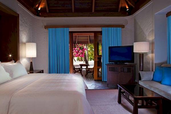 Schlafzimmer im Sheraton Maldives Full Moon Resort & Spa mit einem großen Bett, Fernseher, Lampen und einem offenen Balkon