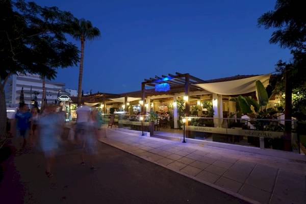 Abendliche Straße vor dem Melissi Beach Hotel & Spa mit Gästen, die vorbeigehen.