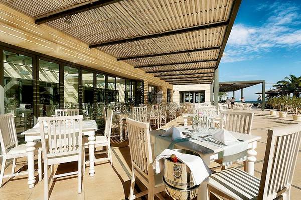 Außenterrasse des Aegean Pearl Hotels mit weißen Tischen und Stühlen und einem Blick auf den Ozean.