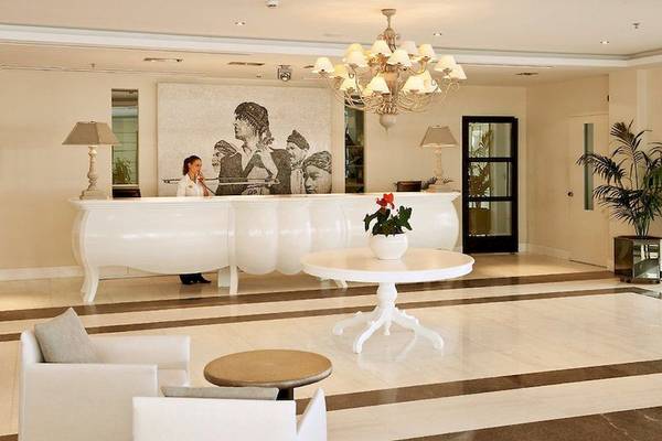 Empfangsbereich des Aegean Pearl Hotels mit weißem Schreibtisch, Stehlampe und Porträtwand