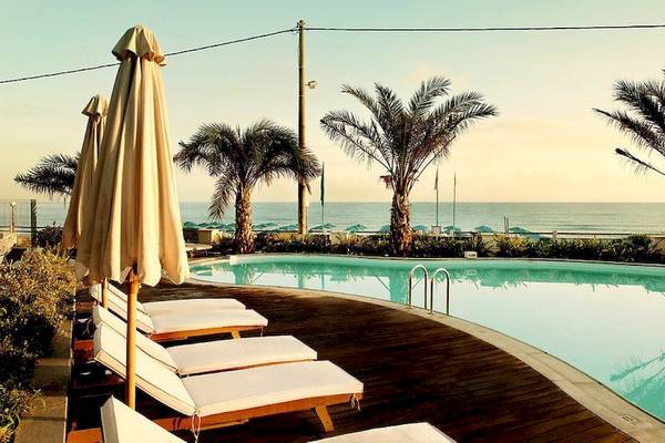 Außenpool des Aegean Pearl Hotels mit Sonnenliegen und Palmen am Strand