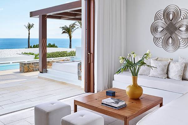 Wohnzimmer im Amirandes Grecotel Boutique Resort mit Blick auf den Ozean und Palmen.